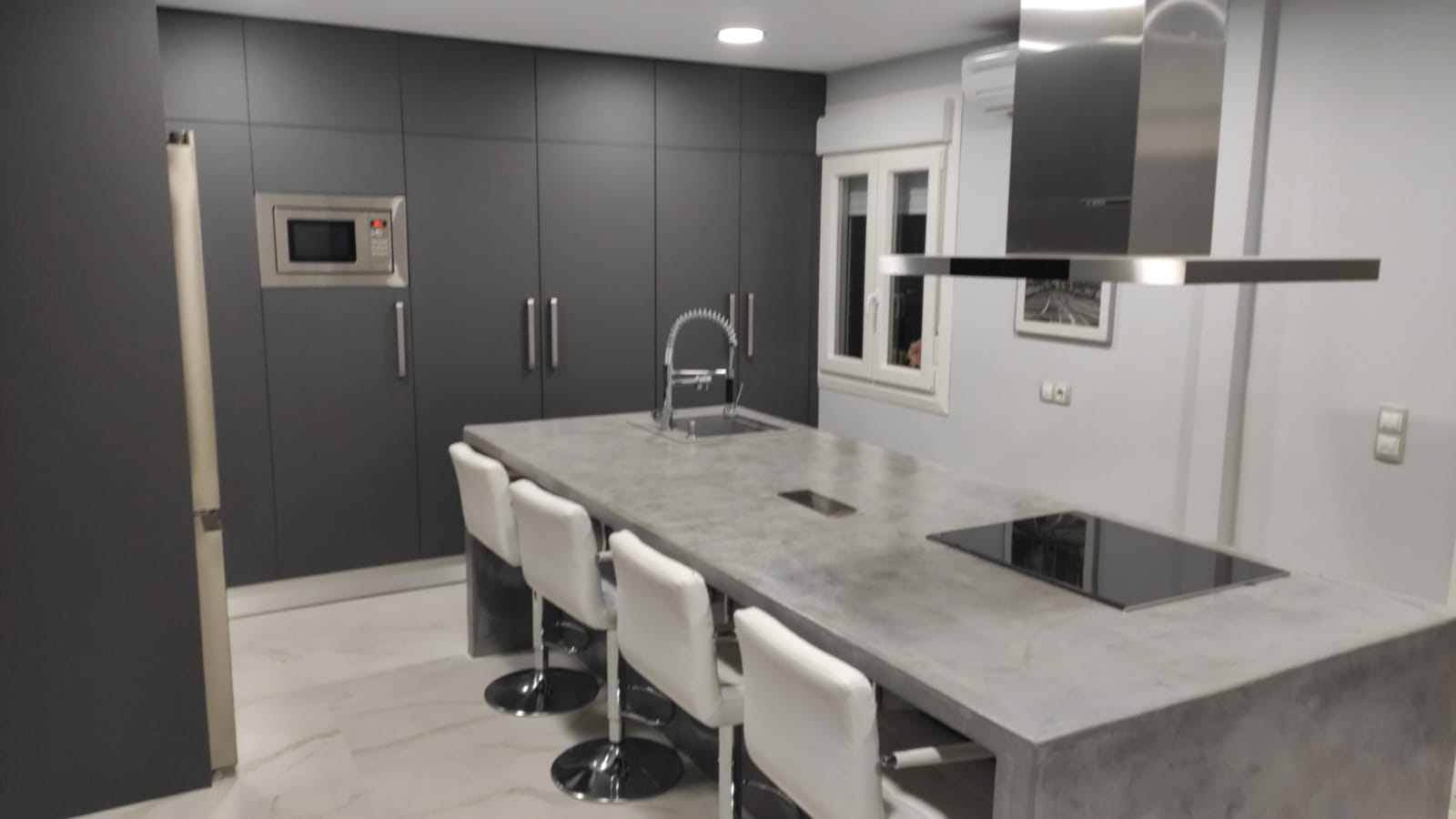 Cocina abierta al salón con armarios grises empotrados e isla con fregadero y vitrocerámica en gris más claro.